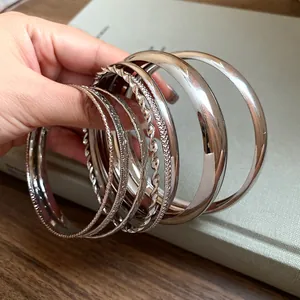 Close-up detail of hand holding a set of textured silver-colored metal bangles for women