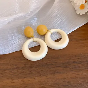 Vista macro di orecchini a cerchio in acrilico crema con borchie a sfera gialle