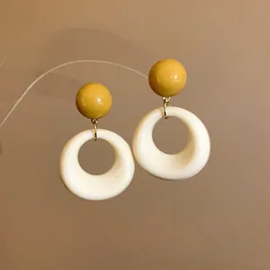 Dettaglio ravvicinato di orecchini pendenti geometrici in acrilico giallo e bianco su supporto