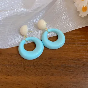 Primo piano di orecchini a cerchio in acrilico azzurro con perni bianco crema su legno