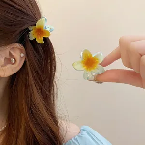 Gros plan sur de mini barrettes à cheveux en forme de fleurs de frangipanier jaune.