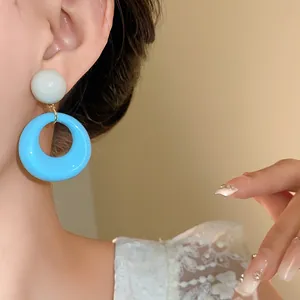 Primo piano di orecchini pendenti rotondi in acrilico azzurro indossati da modella