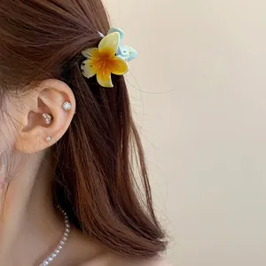Gros plan d'une mini pince à cheveux fleur jaune sur des cheveux bruns avec des accessoires.