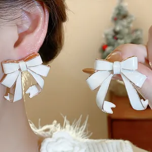 Close-up of white enamel ribbon bow earrings with elegant gold-tone edges