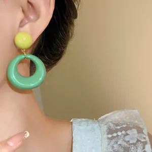 Primo piano di orecchini a cerchio in acrilico verde e giallo su un orecchio di modella