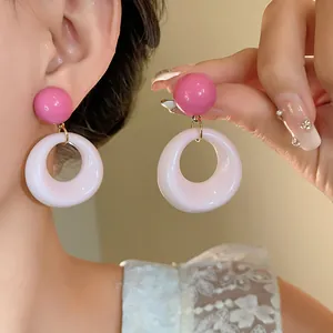 Vista dettagliata di dolci orecchini tondi in acrilico rosa e bianco indossati su