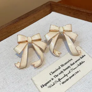 Detailed view of cream enamel bow stud earrings on a vintage textured background