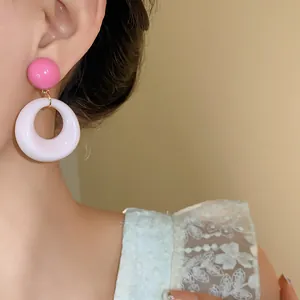 Dettaglio di dolci orecchini pendenti tondi in acrilico rosa e bianco su una modella