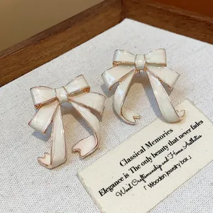 Elegant white enamel bow stud earrings with rose gold trim details for a sophisticated look