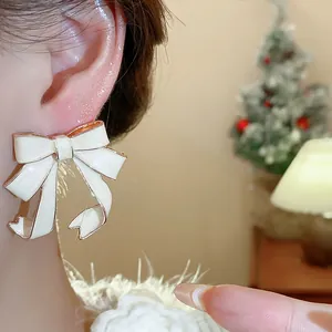 Close-up detail of cream enamel ribbon bow earrings with elegant gold trim
