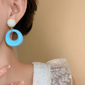 Eleganti orecchini a cerchio in acrilico con ciondolo azzurro mostrati sull'orecchio