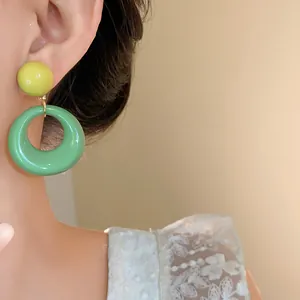 Primo piano di orecchini geometrici in acrilico giallo e verde indossati da modella