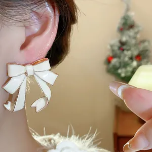 Close-up of cream enamel bow stud earring with gold-toned edges worn by model