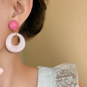 Primo piano di orecchini pendenti tondi in acrilico rosa e bianco sull'orecchio