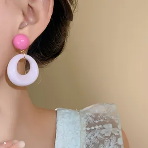 Primo piano di una modella che indossa dolci orecchini a cerchio in acrilico rosa e bianco