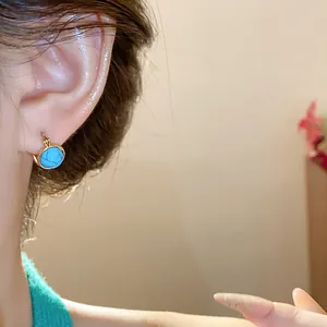 Primer plano de aretes de aro étnicos redondos con resina azul en la oreja del modelo