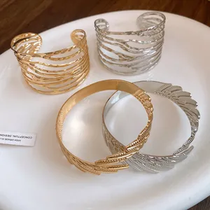 Macro view of gold and silver twisted and feather-style metal cuff bracelets on a white plate