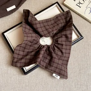 Close-up of a brown plaid fabric scrunchie showing the soft texture and a small bow tag.