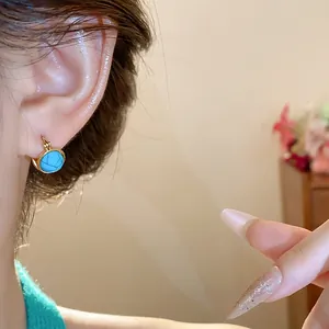 Primer plano de un elegante pendiente redondo vintage dorado con piedra de resina azul
