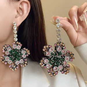Boucles d'oreilles fleurs surdimensionnées avec strass colorés sur l'oreille d'un modèle