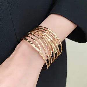 Close-up of a gold twisted feather-textured open cuff bracelet on a wrist.