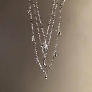 Macro detail showing a layered silver necklace with a sparkling star and a crescent moon.