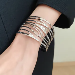 Close-up of a wide silver metal cuff bracelet with a twisted feather cutout design.