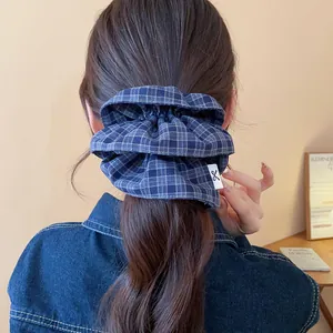 Detail of a large blue plaid fabric scrunchie styled in a low ponytail with denim jacket
