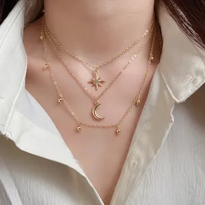 Detail of a three-layer gold necklace with star and moon charms worn with a white shirt.