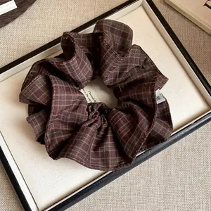 Close-up of a brown grid plaid fabric scrunchie with layered design in a display tray.