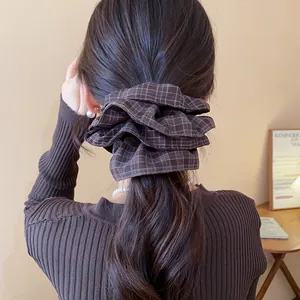 Detail of a brown plaid double-layered fabric scrunchie worn on long wavy hair.