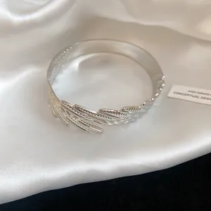 Detailed view of elegant silver feather-shaped open bangle on luxurious white satin.