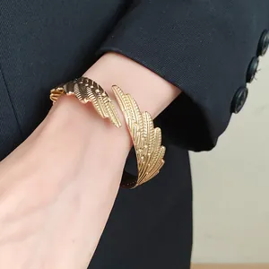 Close-up detail of a vintage golden metal feather open cuff bracelet on a model's wrist