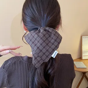 Detail view of a brown plaid fabric scrunchie with handmade label on a ponytail