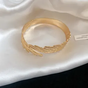 Detailed macro view of vintage gold feather open cuff bracelet on elegant white satin