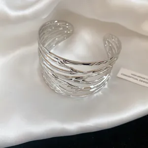 Wide silver metallic open cuff bracelet with intricate twisted feather pattern detail