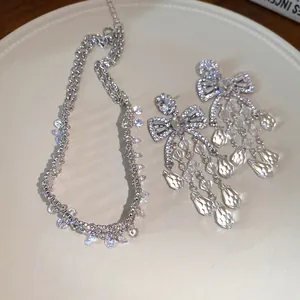 Detailed view of sparkling zircon bow earrings and matching necklace set on a cream plate