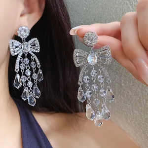Detail view of sparkling bow chandelier earrings with crystal drop tassels worn by model