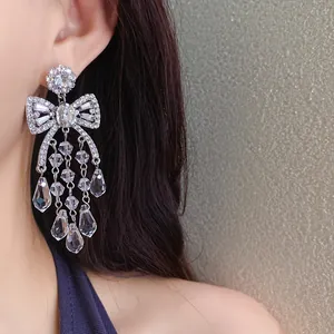 Close-up detail of sparkling silver bow earrings with dangling teardrop crystals