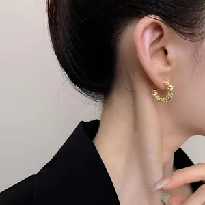 Detail view of textured gold geometric C-shaped hoop earring worn by an Asian model
