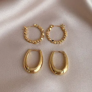 Elegant set of two gold-plated geometric hoop earrings on champagne satin background