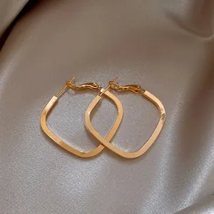 Close-up of elegant gold geometric hoop earrings on satin background