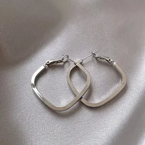 Macro view of geometric silver square hoop earrings on an elegant silk background