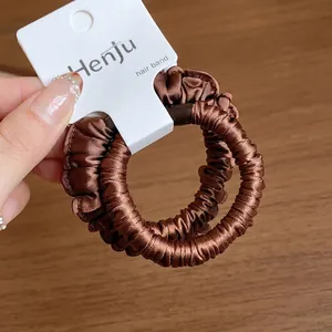 Dark brown pleated fabric hair scrunchie with elastic band shown on a white hangtag