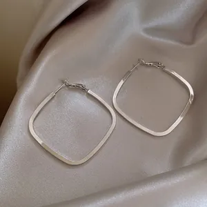 Close-up macro view of elegant polished silver square hoop earrings on champagne silk fabric