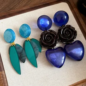 Vue de boucles d'oreilles en résine avec motifs de cœur, rose et feuille sur plateau de lin.