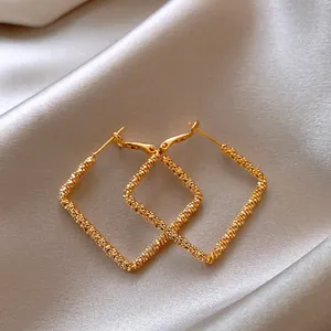 Detailed macro view of gold square hoop earrings with unique spiral textured metal design