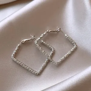 Close-up of silver-colored square hoop earrings with textured ribbed surface on satin