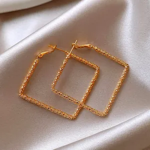 Detailed view of golden square geometric earrings with textured wire-wrapped design
