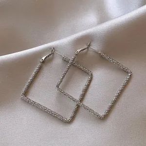 Detailed view of textured silver square hoop earrings on elegant satin fabric